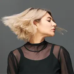 Kobieta z blond włosami w ruchu, w czarnej, prześwitującej bluzce. Efekty stylizacji fryzury.