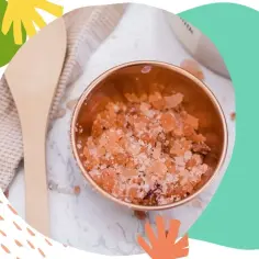 Różowy peeling do ciała w miedzianej miseczce, obok drewnianej szpatułki i lnianej ściereczki. Idealny do domowego SPA.