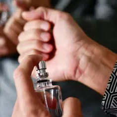 Dłoń trzyma flakonik perfum, psikając na nadgarstek. To klasyczny sposób, gdzie psikać perfumy, by zapach utrzymywał się dłużej.