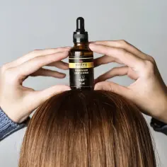 Dłonie trzymają buteleczkę z serum do włosów Sattva Ayurveda. Czy serum do włosów się spłukuje? To pytanie zadaje sobie wiele osób.