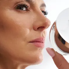 Kobieta z uwagą przygląda się bronzerowi, szukając sposobu, jak zmniejszyć nos makijażem.