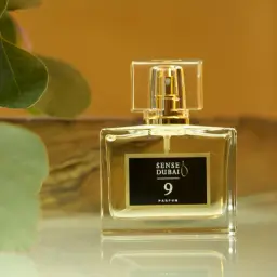 Eleganckie perfumy damskie z Dubaju, Sense Dubai 9 Parfum, w szklanym flakonie z złotymi detalami, otoczone zielonymi liśćmi.