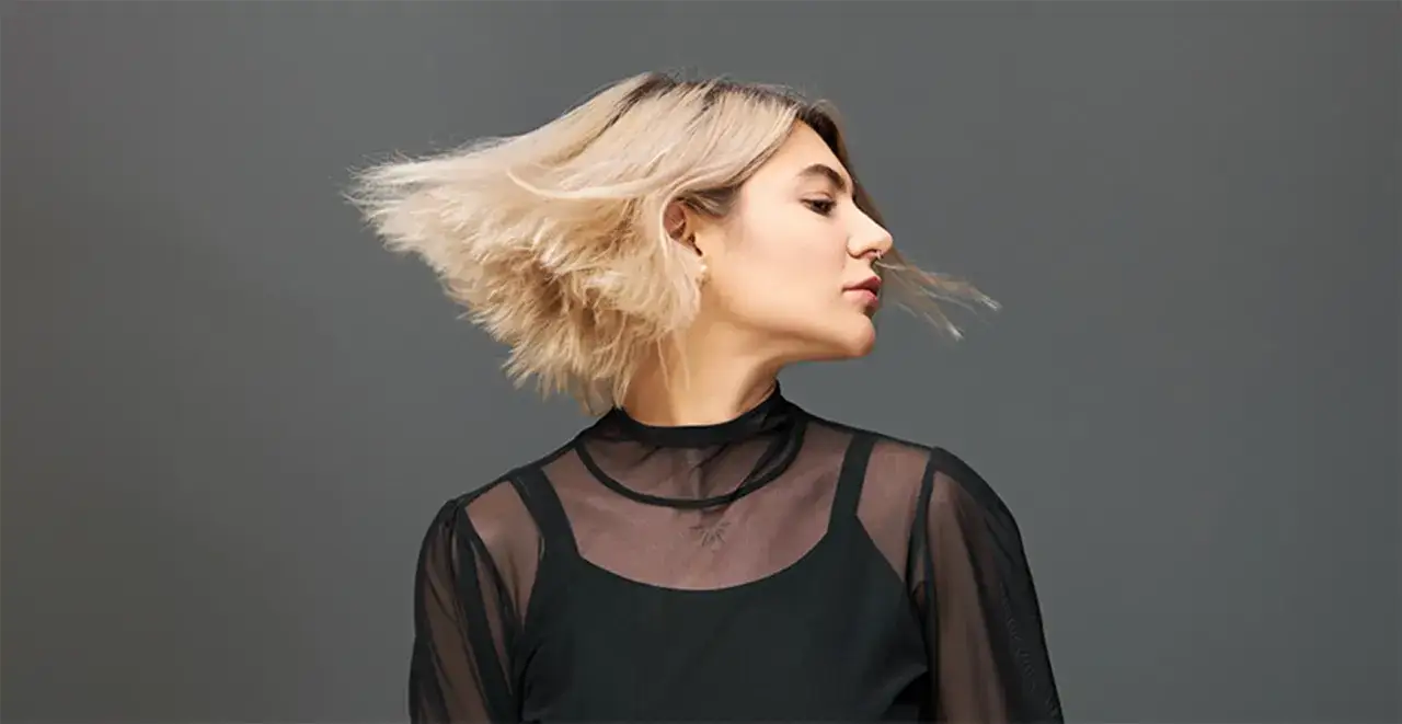 Kobieta z blond włosami w ruchu, w czarnej, prześwitującej bluzce. Efekty stylizacji fryzury.