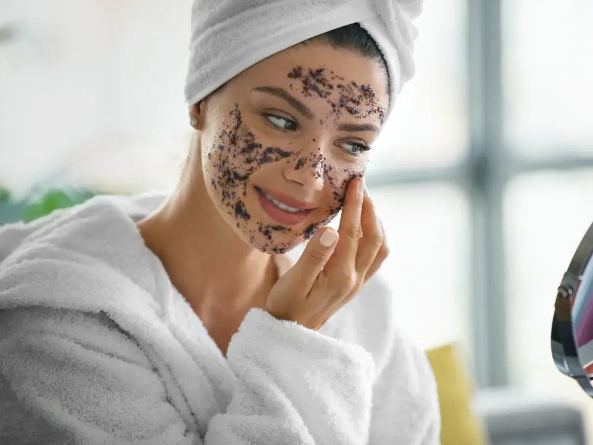Kobieta w szlafroku i ręczniku na głowie nakłada na twarz domowy peeling. To świetny sposób, jak zrobić domowy peeling do twarzy.