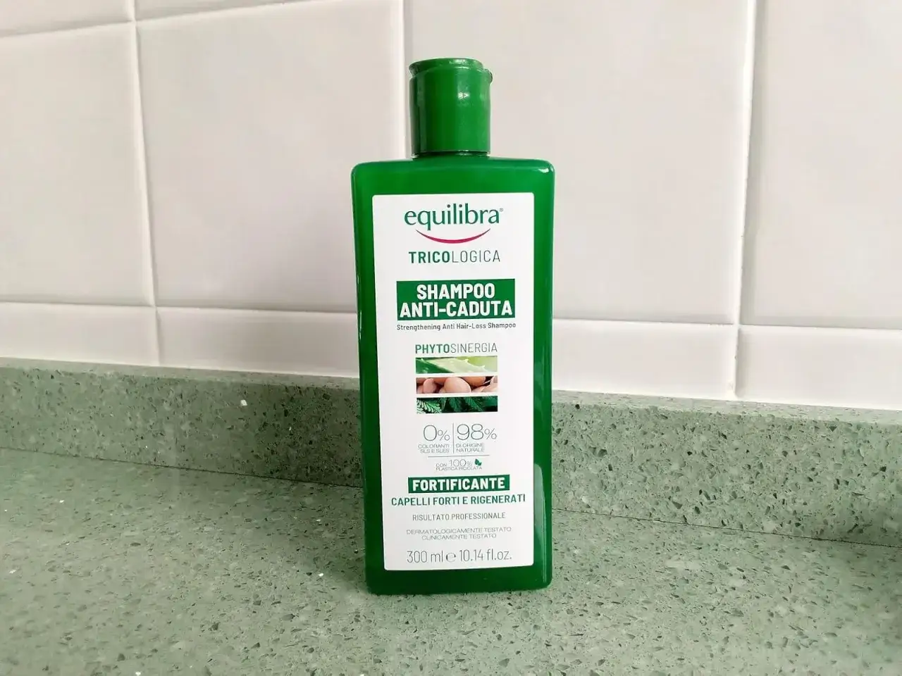 Zielona butelka szamponu Equilibra Tricologica Shampoo Anti-Caduta, który jest szamponem na wypadanie włosów, stoi na blacie.