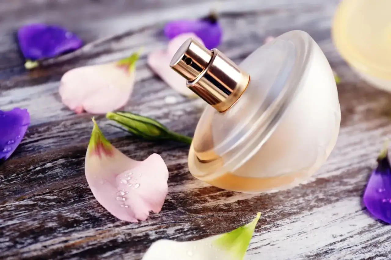 Elegancka butelka perfum na drewnianym blacie, otoczona płatkami różowych i fioletowych kwiatów. Jak napełnić perfumy?
