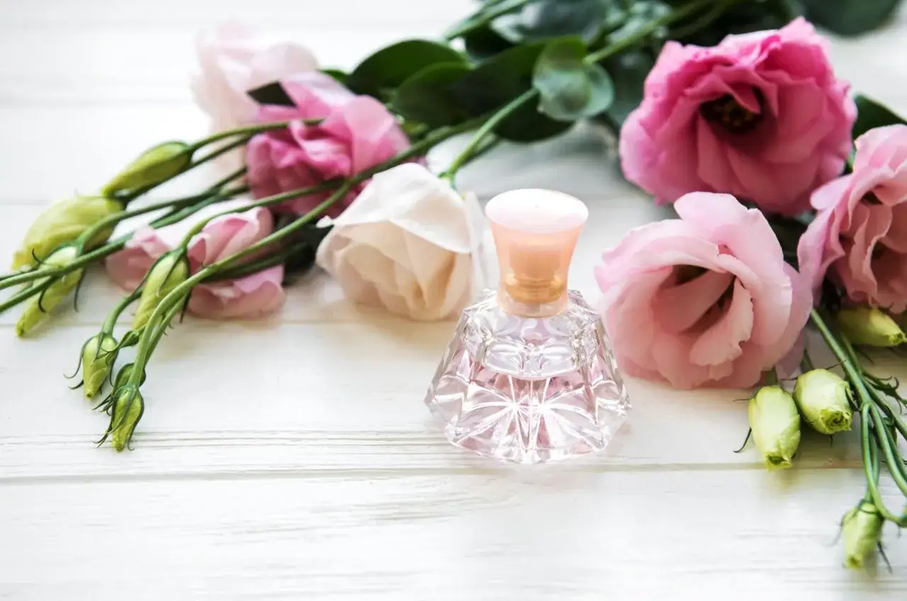 Delikatna buteleczka perfum wśród różowych kwiatów. Inspiracja, jak zrobić perfumy z kwiatów.