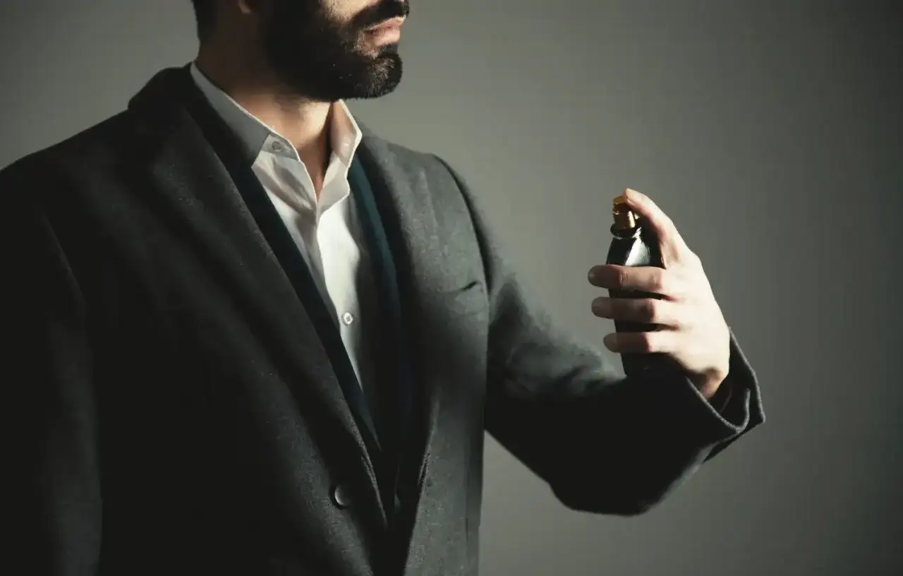 Elegancki mężczyzna w garniturze psika perfumy na nadgarstek. Właściwe miejsca, gdzie psikać perfumy, podkreślają jego styl.